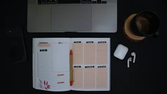 A weekly planner open next to a laptop and a coffee