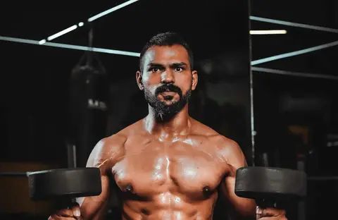 A muscular man holding two dumbbells at shoulder height