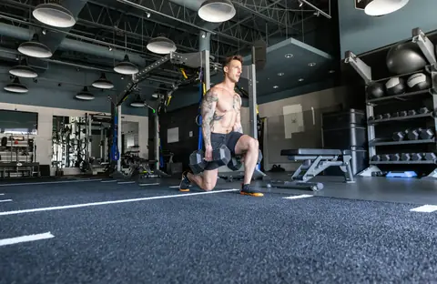 A man doing a dumbbell lunge in a gym