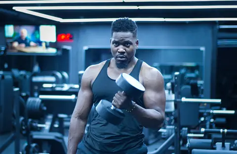 A muscular man curling a heavy dumbbell in a dark gym