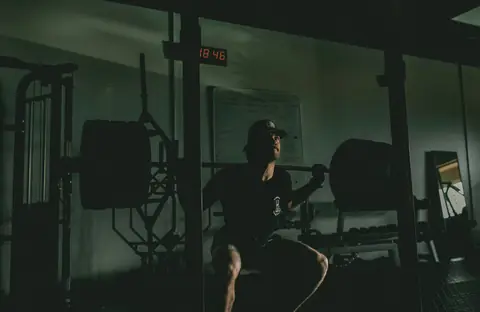 A man training in a dark gym at a squat rack